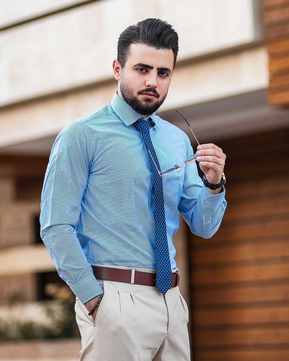 man in blue dress shirt and white pants holding black sunglasses